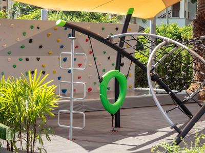 Nowoczesny plac zabaw na zewnątrz z ścianką wspinaczkową, zieloną huśtawką i roślinami pod daszkiem