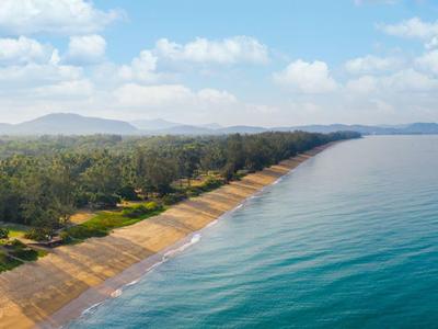 Długa piaszczysta plaża z falami, otoczona zieloną roślinnością i górami w tle.