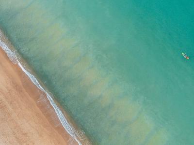 Widok z powietrza na plażę z niebieską wodą i małą łodzią
