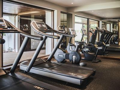 Nowoczesna siłownia z bieżniami i rowerkami stacjonarnymi przed dużymi oknami.