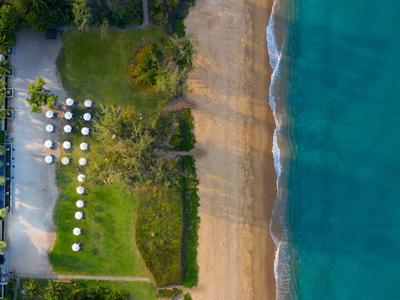 Widok z lotu ptaka na plażę z przyległym terenem hotelowym i turkusowym morzem.