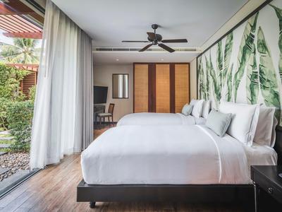 Nowoczesny pokój hotelowy z dwoma łóżkami, wentylatorem sufitowym i dostępem do ogrodu przez duże szklane okna.