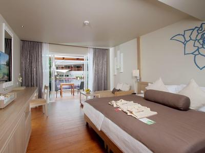 Camera d'hotel moderna con letto matrimoniale, pavimento in legno e balcone con zona salotto e vista mare.