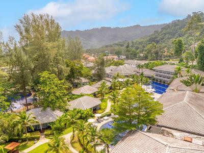 Aerial view of a resort with a pool, bungalows, and green trees against mountains