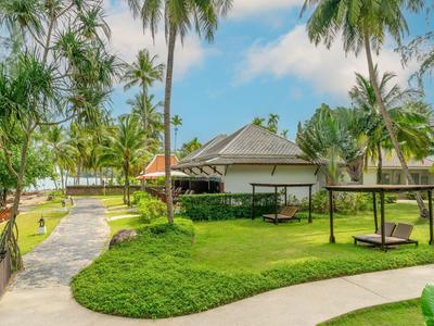 Bungalow omgeven door palmbomen en gras in tropisch resort onder zonnige lucht.