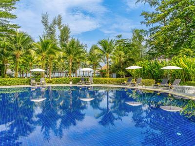 Round pool with blue water, palm trees, and sun umbrellas in a tropical hotel garden.
