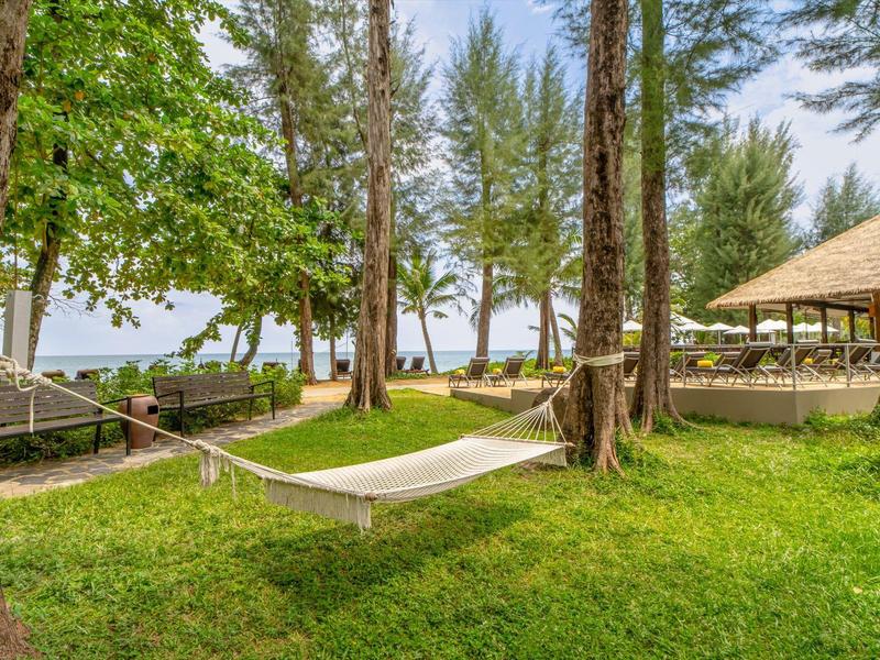 Hangmat tussen bomen op groen gras met uitzicht op zee en paviljoen.