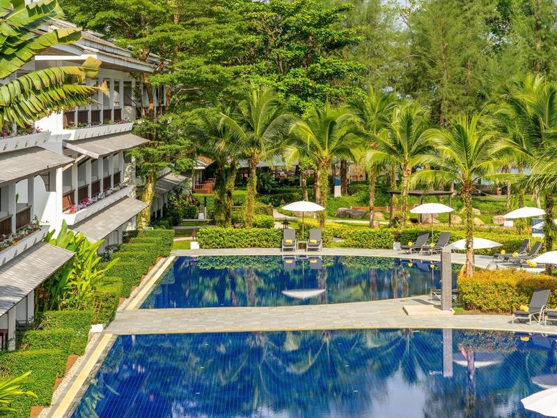 Een hotel met een groot zwembad, groene tuinen en veel palmbomen.