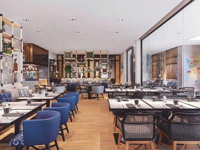 Moderner Restaurantinnenraum mit Holzboden, blauen Sesseln und großen Fenstern.