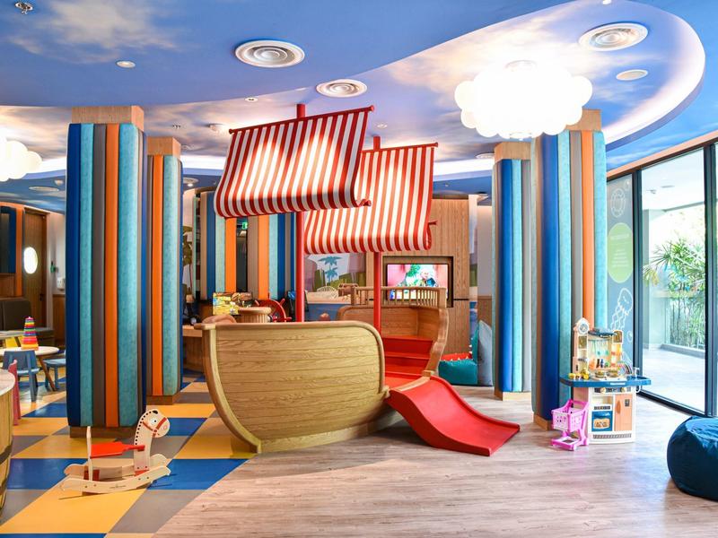 Kolorowy plac zabaw dla dzieci z łodzią, zjeżdżalnią i nowoczesnymi miejscami do siedzenia w jasnym pomieszczeniu.