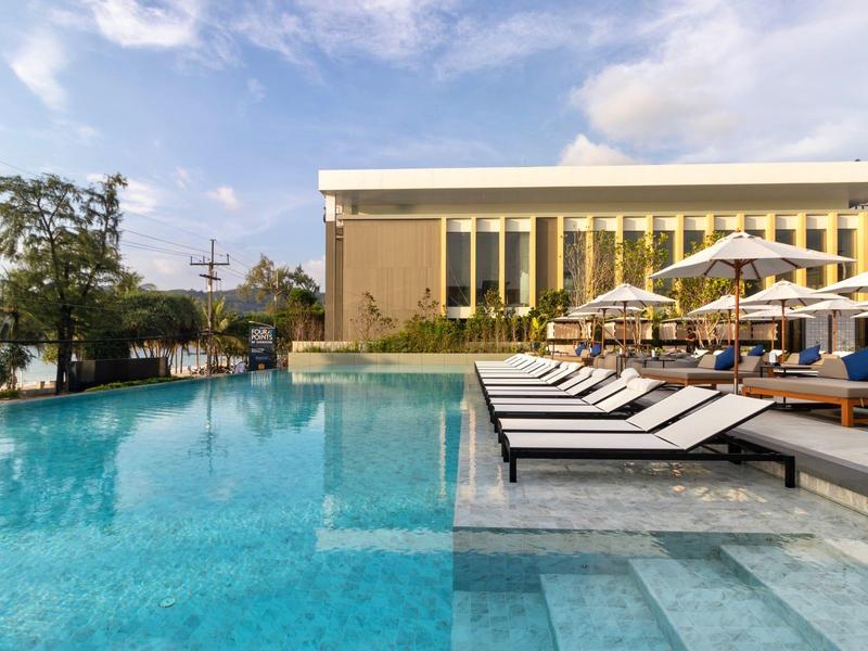 Nowoczesny basen na zewnątrz z leżakami i parasolami obok budynku pod czystym niebem.