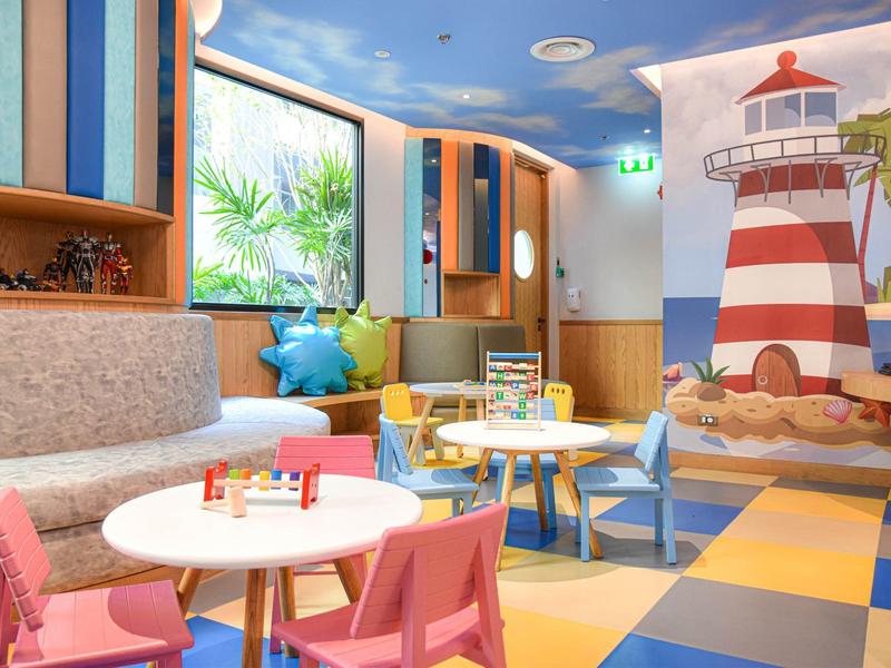 Kolorowy, nowoczesny kącik zabaw dla dzieci z małymi stołami, krzesłami i muralem latarni morskiej.