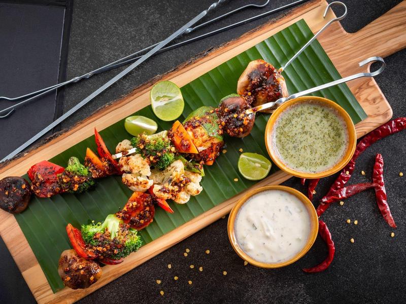 Różne grillowane szaszłyki z sosami i limonką na drewnianej desce z liściem bananowca.