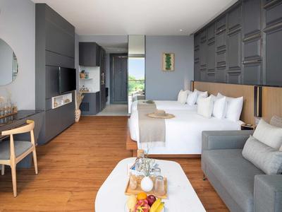 Camera d'hotel moderna con letto matrimoniale, zona soggiorno e pavimento in legno.