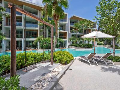 Modern hotel pool area with loungers, umbrellas, and greenery under clear skies.