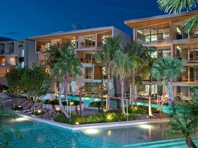 Vista notturna di un hotel con piscina illuminata e palme.