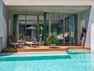 Piscina di hotel moderna con sedie a sdraio e pianta accanto a porte scorrevoli in vetro a tutta altezza.