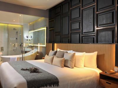 Camera d'hotel moderna con letto grande e bagno aperto con vasca da bagno e doccia.