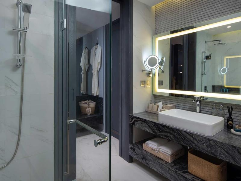 Bagno d'hotel moderno con specchio illuminato, lavabo e doccia walk-in.