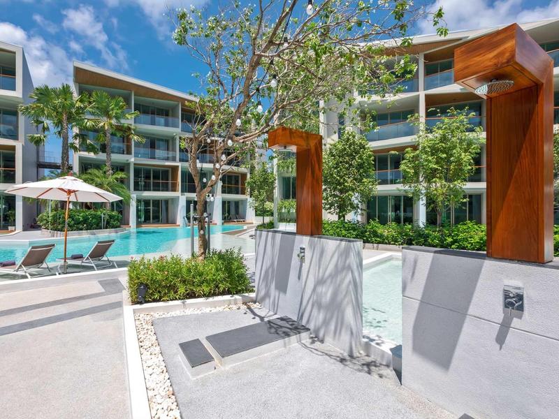 Docce esterne moderne con soffioni marroni accanto a una piscina e lettini in un complesso alberghiero.