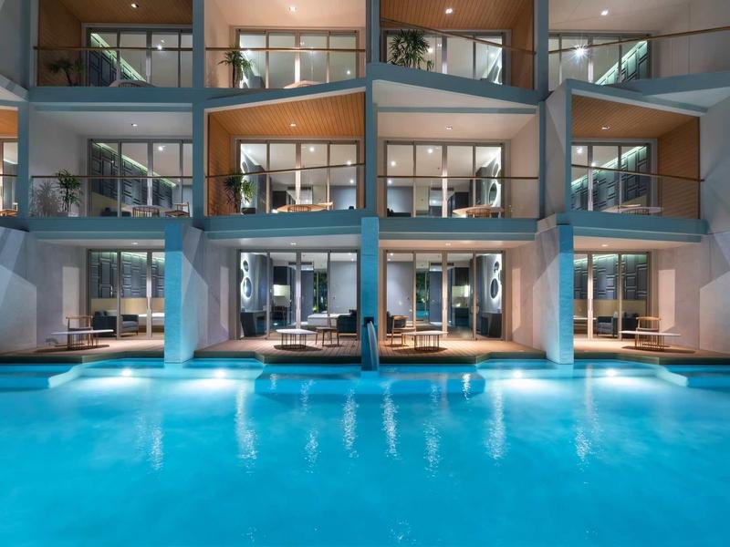 Vista notturna di un hotel con camere illuminate e una grande piscina all'aperto.