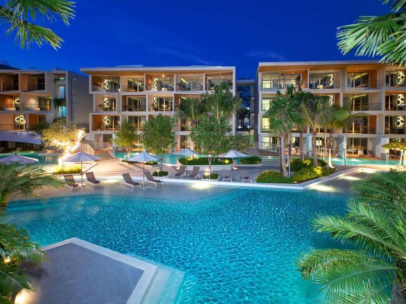 Complesso alberghiero moderno con piscina illuminata e vegetazione tropicale di notte.