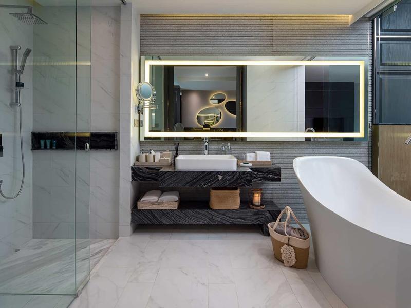 Bagno moderno con vasca freestanding, grande specchio illuminato e cabina doccia in vetro.