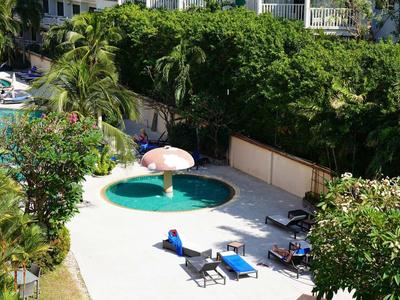 Piccola piscina rotonda con lettini e ombrellone, circondata da alberi ed edifici.