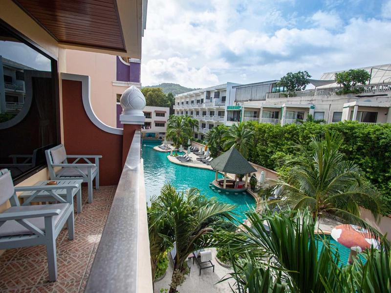 Vista da un balcone con sedie su una piscina tropicale dell'hotel e gli edifici circostanti.