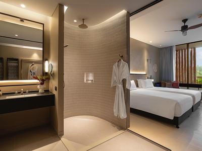 Habitación de hotel moderna con dos camas, baño contiguo y grandes ventanas con vista al verde.