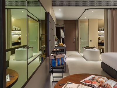 Habitación de hotel moderna con ducha de vidrio, cama, mesa y silla en tono cálido.