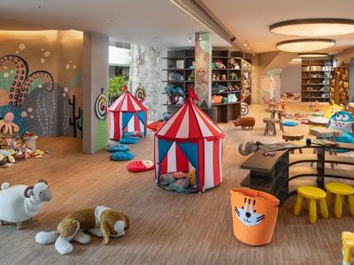 Sala de juegos infantil luminosa con carpas coloridas, figuras de animales y suelo blando en un vestíbulo de hotel.