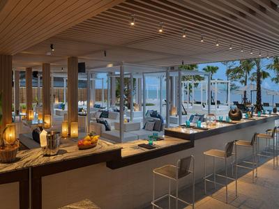 Área moderna de bar en el hotel con asientos y vista a la terraza y al mar.