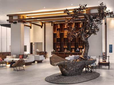 Gran vestíbulo de hotel con mobiliario moderno y árbol escultórico en el centro.
