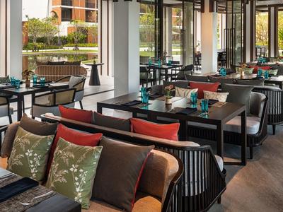 Restaurante moderno con áreas de asiento acogedoras, mesas de madera y cojines coloridos en un espacio luminoso.