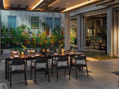 Área de comedor exterior moderna con mesas, sillas y un mural colorido en un hotel.