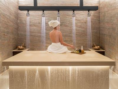 Persona sentada en una cama de spa moderna con chorros de agua desde arriba.