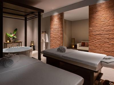 Sala de spa moderna con dos camillas, bañera de bienestar y luz tenue en tonos cálidos.