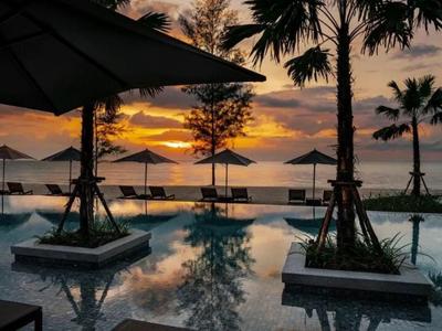 Sunset over a pool with palm trees and umbrellas by the sea