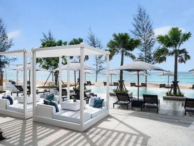 Modern bright outdoor area with white lounge beds, chairs, and palm trees by the beach.