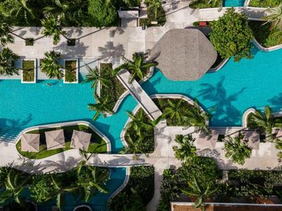 Vista aérea de una piscina de hotel con puentes rodeada de palmeras y áreas verdes.