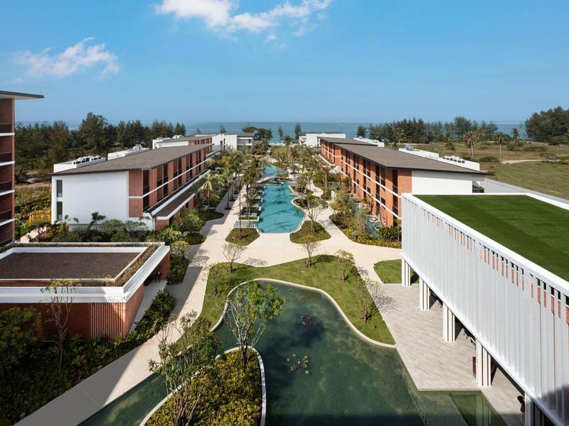 Complejo hotelero moderno con piscina y áreas verdes, rodeado de naturaleza y vista al mar.