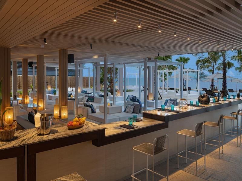 Área moderna de bar en el hotel con asientos y vista a la terraza y al mar.