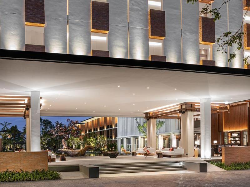 Entrada moderna de hotel con techo iluminado y área de recepción acogedora al atardecer.