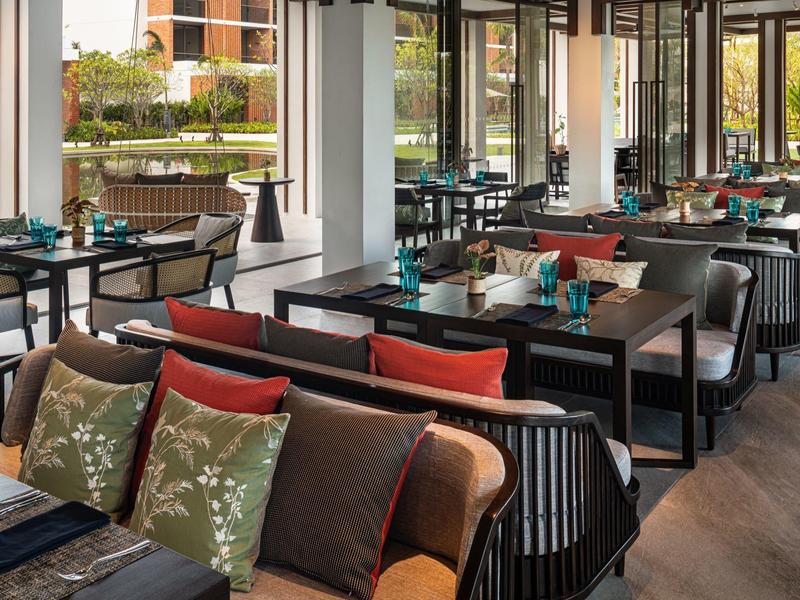 Restaurante moderno con áreas de asiento acogedoras, mesas de madera y cojines coloridos en un espacio luminoso.