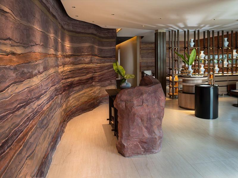 Recepción de hotel elegante con un revestimiento de madera ondulada y una recepción de piedra única.