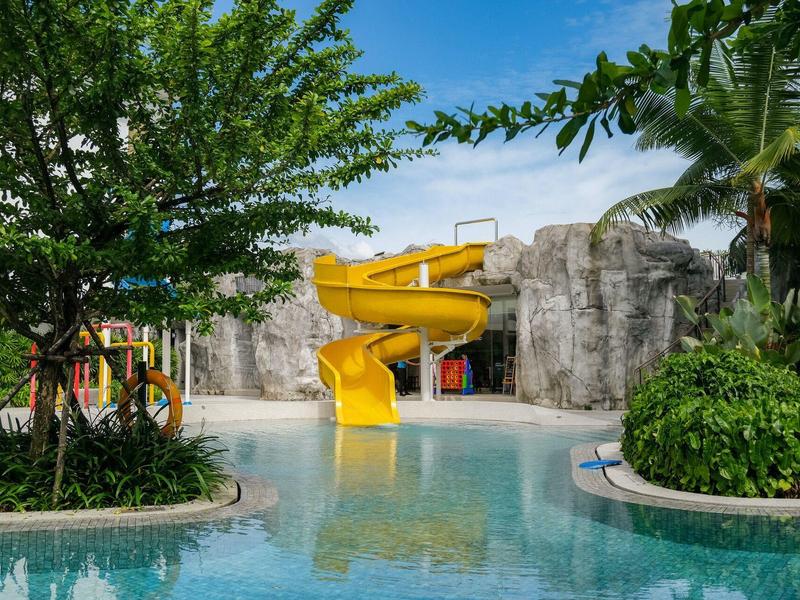 Tobogán de agua amarillo en una piscina rodeada de vegetación tropical y rocas.