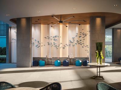 Nowoczesna lobby hotelowa z dużym wentylatorem sufitowym, instalacją artystyczną i poduszkami do siedzenia.