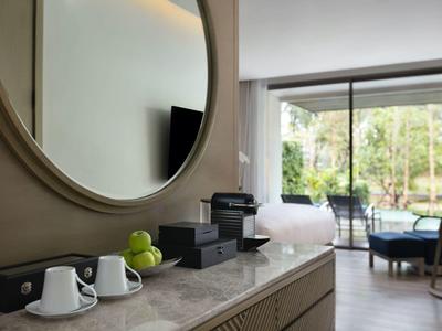 Nowoczesny pokój hotelowy z lustrem, ekspresem do kawy i widokiem na taras z meblami ogrodowymi.