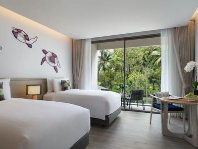 Słoneczny taras hotelowy z drewnianym stołem, mieszanymi krzesłami i bujną zielenią roślin.